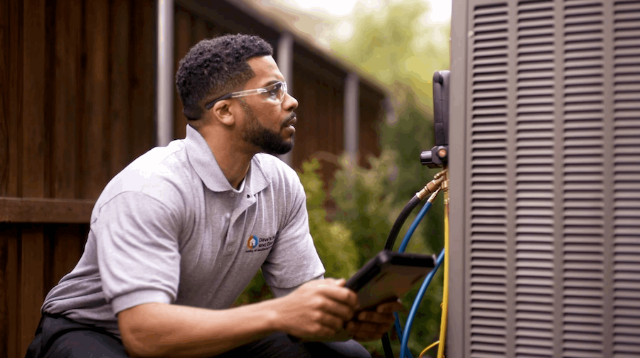 Technician inspecting an outdoor AC unit with diagnostic equipment