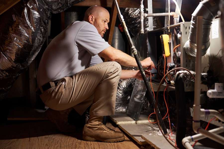 Technician repairing HVAC equipment in an attic space